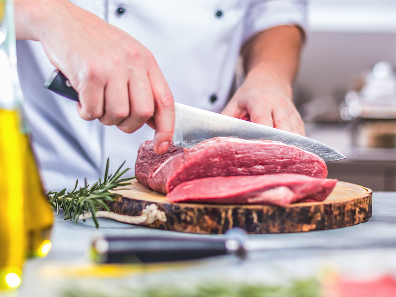 Nahaufnahme von den Händen eines Fleischers. Er schneidet ein Stück Fleisch.